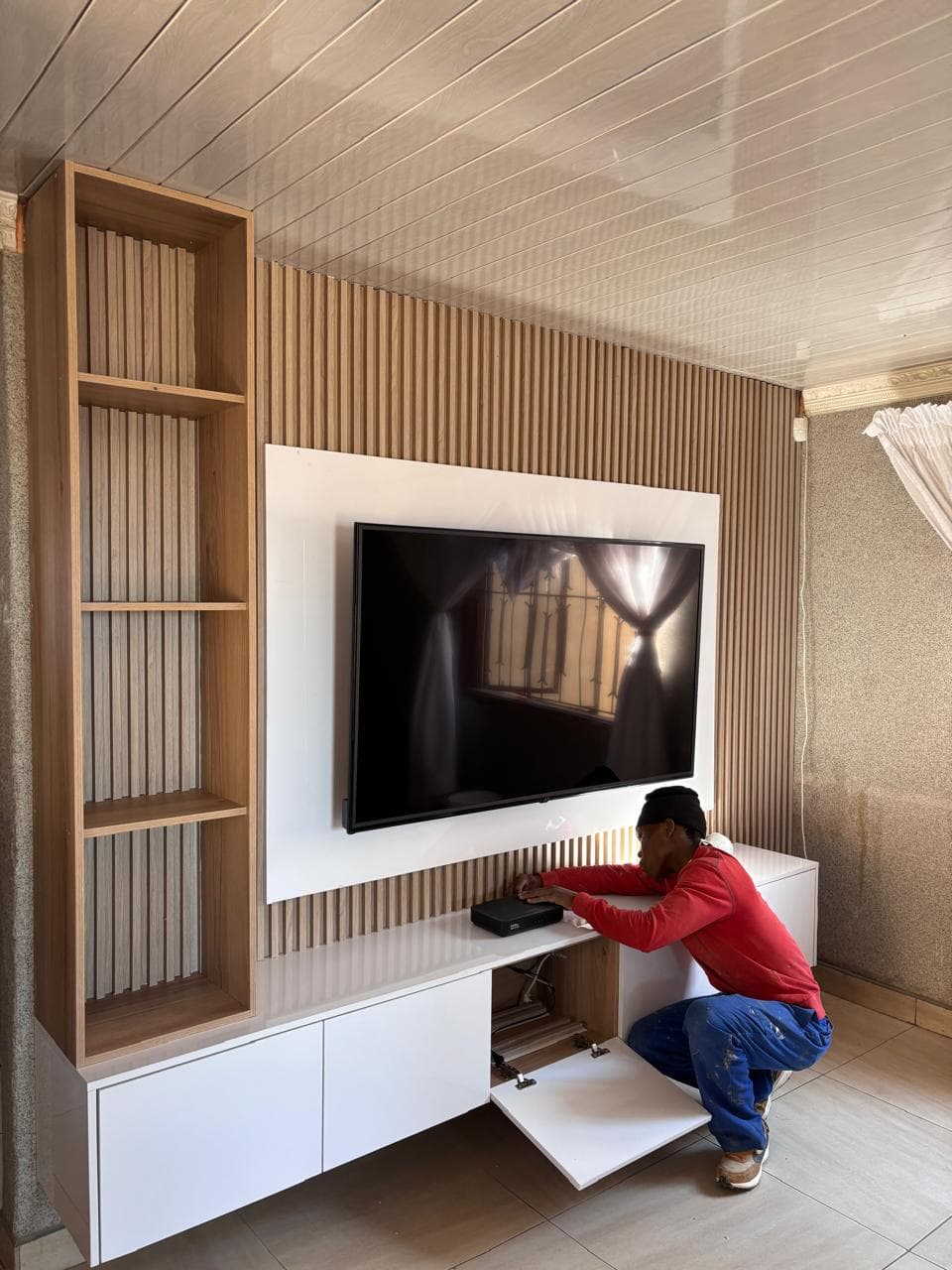Fitter installing a light oak TV wall unit and floating console